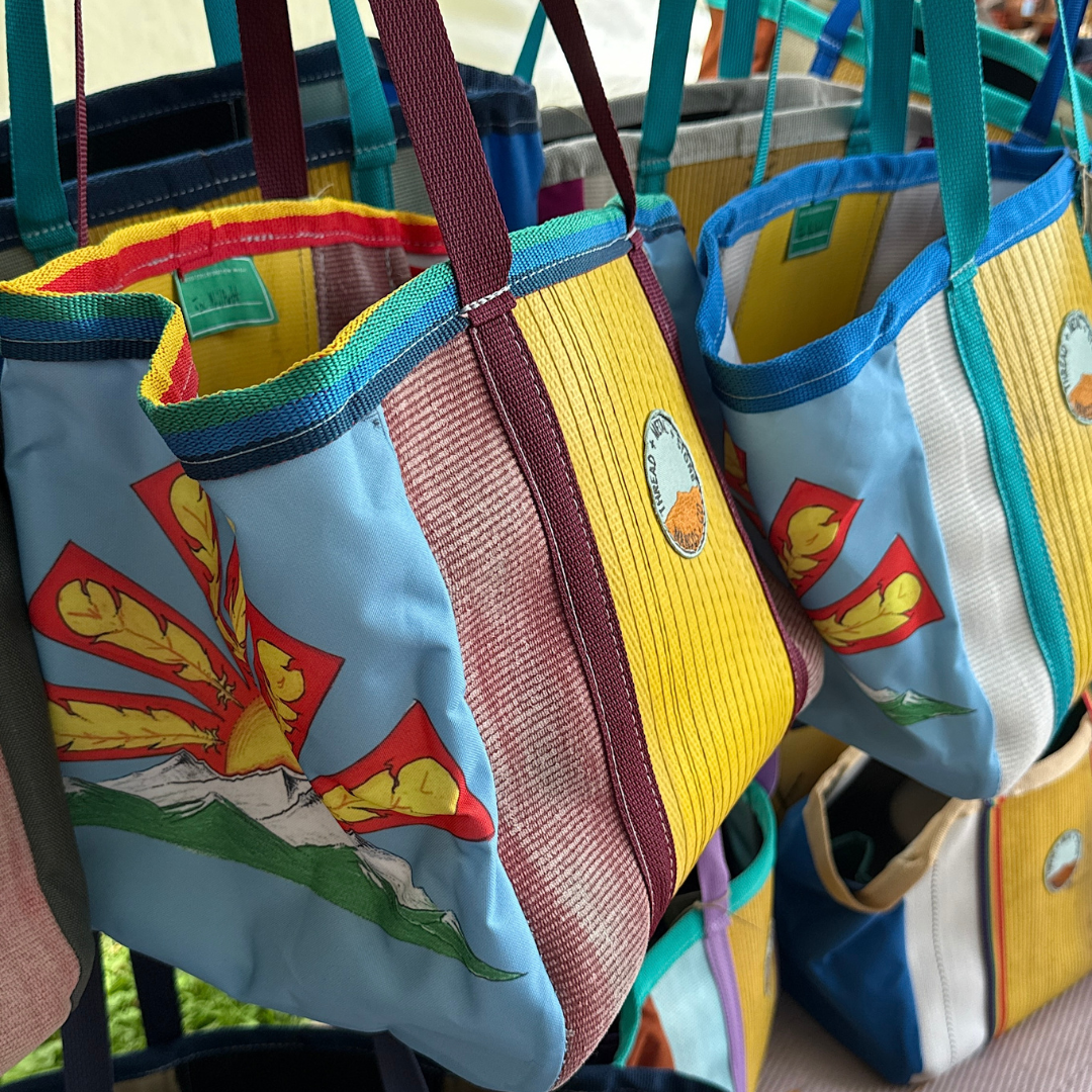 A close-up of a fire hose tote bag featuring a design by Joe Philpott, with light blue, yellow, red, white, and green panels and teal handles.